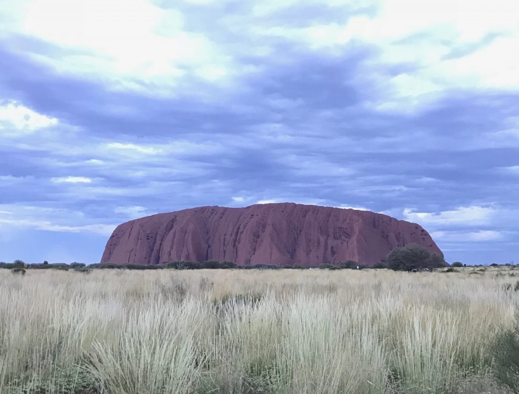 Molly from Mollywozhere travel blog showing the beautiful Uluru Rock with blue sky and white clouds, Australia's Red Centre.
