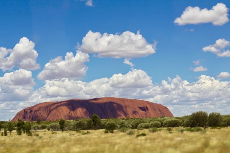 Molly from Mollywozhere travel blog showing the beautiful Uluru with blue sky and white clouds, Australia's Red Centre
