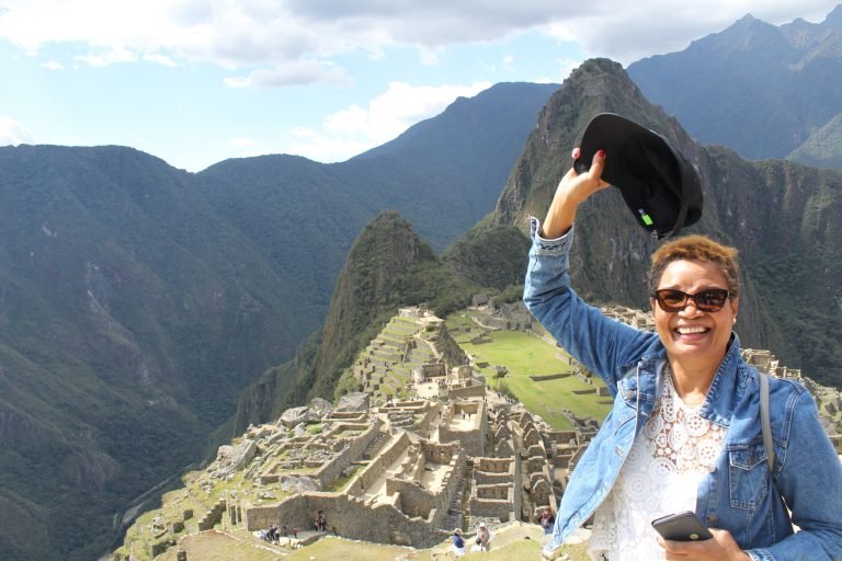 Molly from Mollywozhere travel blog standing at the top of Machu Picchu, Peru waving her hat in joy.