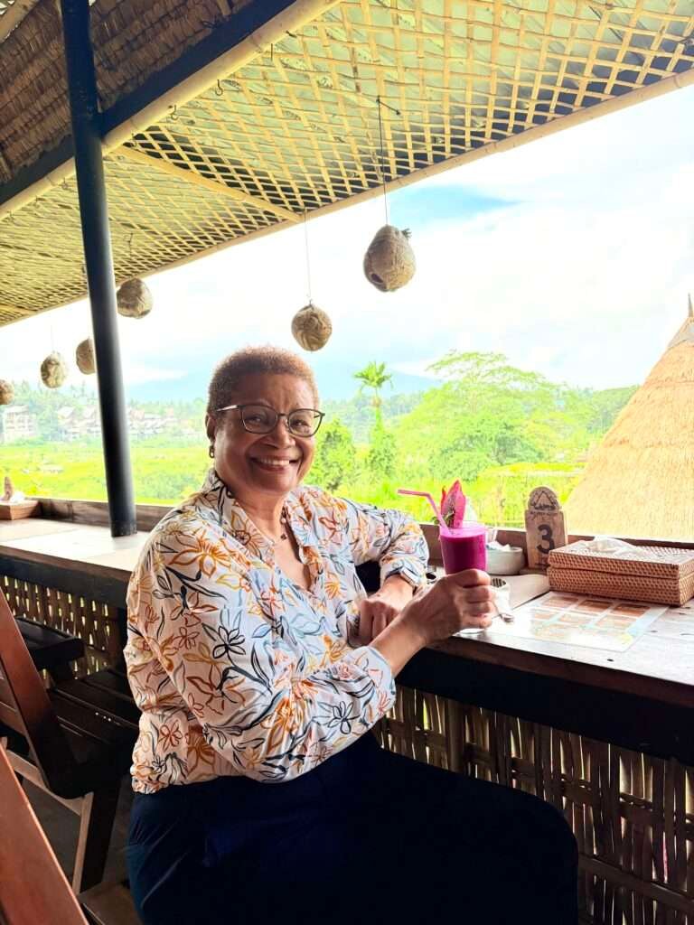Molly from Mollywozhere travel blog showing a glass of strikingly vibrant magenta Balinese dragon fruit juice on a table in Bali.
