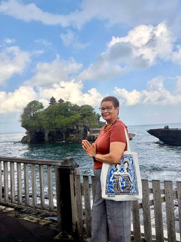 Molly from Mollywozhere travel blog standing in front of a wooden fence looking at Tanah Lot temple, Bali.