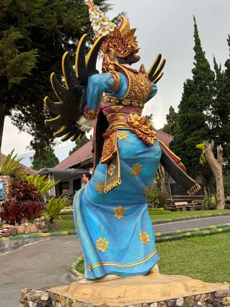 Molly from Mollywozhere looking at the statue of a dancer dressed in blue traditional dress in Ulun Danu Beratan Temple,Bali.