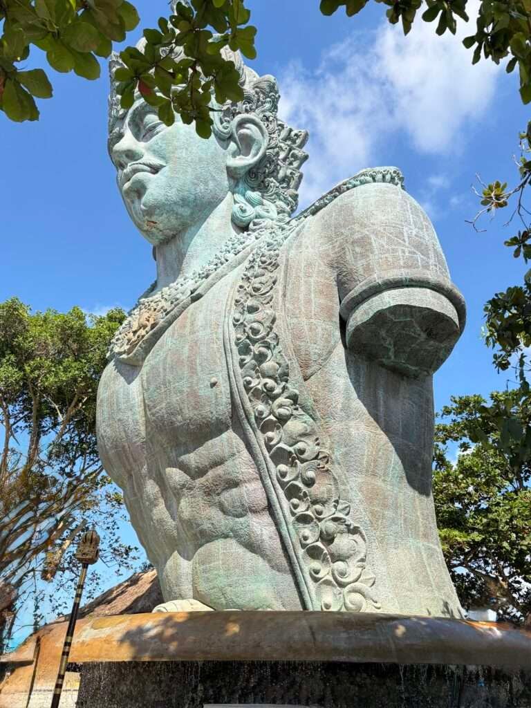 Molly from Mollywozhere travel blog looking at a close up of a massive sculpted stone head leaning forward at the top of GWK Cultural Park, Bali.
