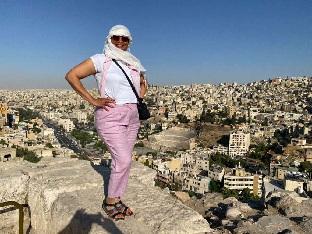 Molly from Mollywozhere travel blog standing on a ledge and looking across to Amman Citadel, Jordan.