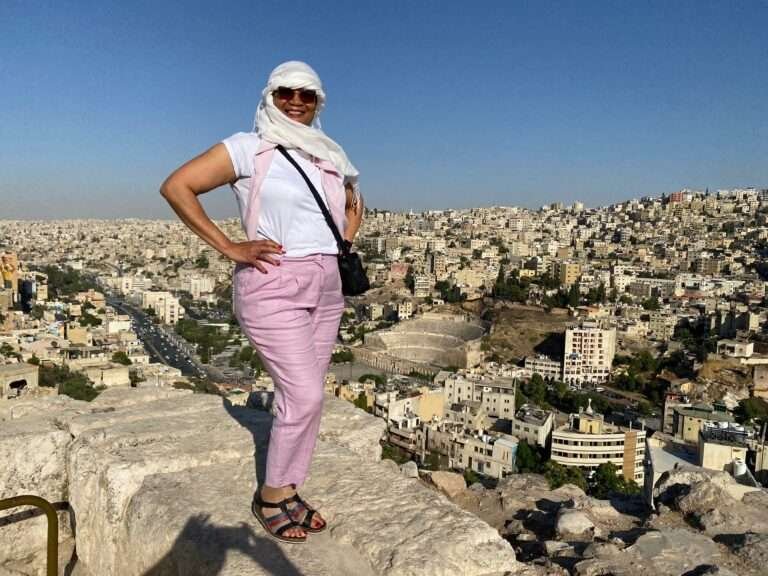 Molly from Mollywozhere travel blog standing on a ledge and looking across to Amman Citadel, Jordan.